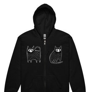 Puede incluir: Sudadera negra con cremallera y capucha, con un gráfico blanco de dos gatos estilizados en la parte delantera. Los gatos miran en direcciones diferentes.