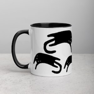 May include: White ceramic mug with a black rim and handle. The mug features a black and white illustration of four cats in different positions.