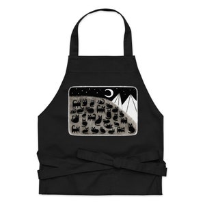 May include: Black apron with a white pocket featuring a black and white illustration of a mountain range with a crescent moon and a group of black cats.