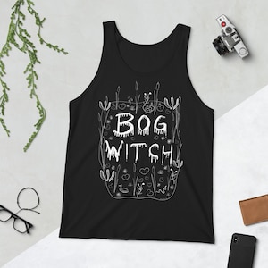 Puede incluir: Camiseta de tirantes negra con un gráfico blanco de un pantano con el texto "BOG WITCH" en letras blancas que gotean.