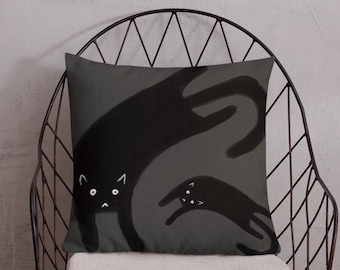Puede incluir: Una almohada gris con una ilustración en blanco y negro de dos gatos. El gato más grande está de pie sobre sus patas traseras y el gato más pequeño está sentado frente a él.