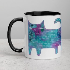 May include: A white ceramic mug with a black rim and handle. The mug features a watercolor illustration of a blue and purple cat with a white outline.