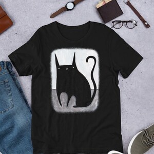 May include: Black t-shirt featuring a graphic of a black cat sitting on a grey background.