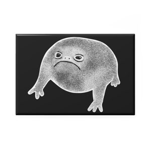 May include: A rectangular black magnet featuring a grayscale illustration of a sad, blob-like creature with small arms and a downturned mouth. The creature has a textured appearance and is set against a solid black background.