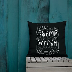 May include: Black throw pillow with white text that reads "Swamp Witch" and a design of swamp creatures and plants.
