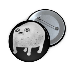 May include: A black and white button featuring a cartoon illustration of a white, round, furry creature with large eyes and a small mouth. The creature has four short legs and is standing on a black background.