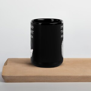 May include: Black ceramic mug with white text and a cat illustration. The mug reads "I'm the head must look how". The mug is displayed on a wooden surface.