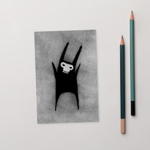 May include: A black and white illustration of a creature with a skull-like face and raised arms. The artwork is on a gray rectangular card, accompanied by two pencils, one green and one teal.