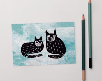 Op de afbeelding: Twee zwarte katten met witte glimlachende gezichten zitten op een lichtblauwe achtergrond. De katten zijn getekend in een eenvoudige, cartoonachtige stijl.