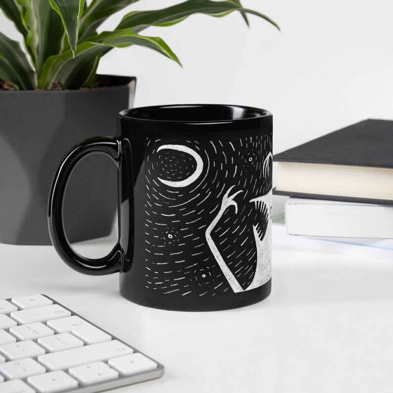 Pode incluir: Caneca de cer&acirc;mica preta com uma ilustra&ccedil;&atilde;o branca de uma criatura sob uma lua crescente e estrelas. A caneca tem uma al&ccedil;a preta e um acabamento brilhante. O design &eacute; uma representa&ccedil;&atilde;o art&iacute;stica e caprichosa de uma cena noturna.