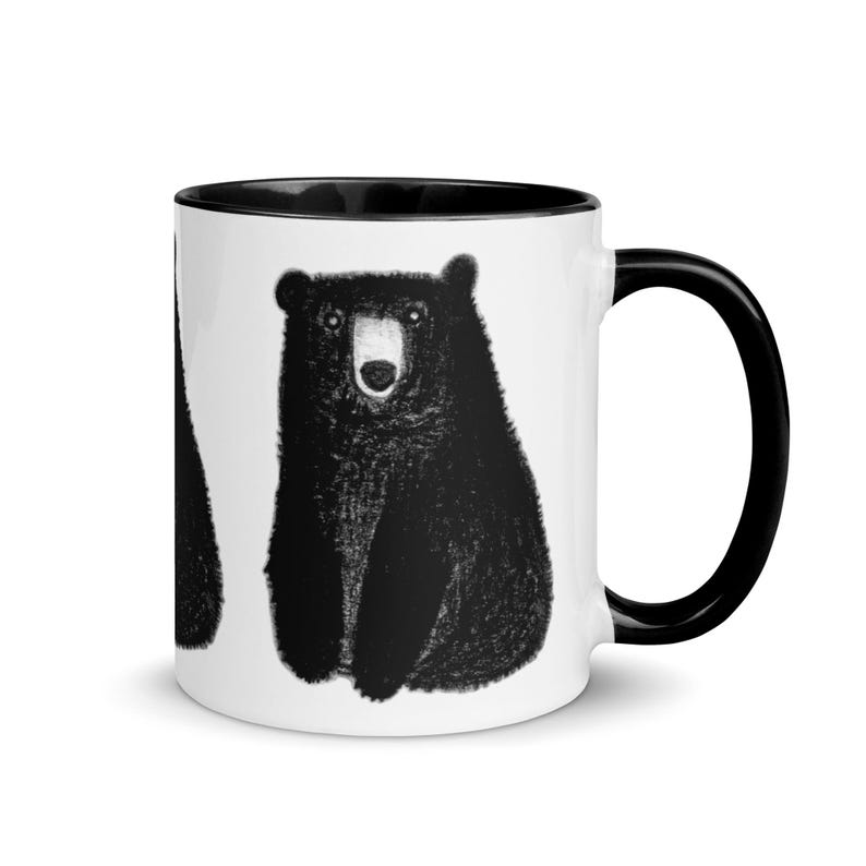 May include: White ceramic mug with a black rim and handle. The mug features a black and white illustration of a bear.