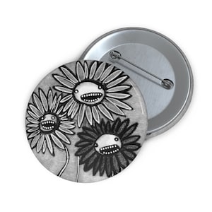 May include: A round button with a grayscale illustration of three cartoon sunflowers with toothy grins. The button is silver-colored on the back with a pin. The sunflowers have detailed petals and stems against a gray background.