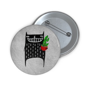 May include: A black cat with a big smile holds a potted plant with green leaves. The cat is standing on a gray background.