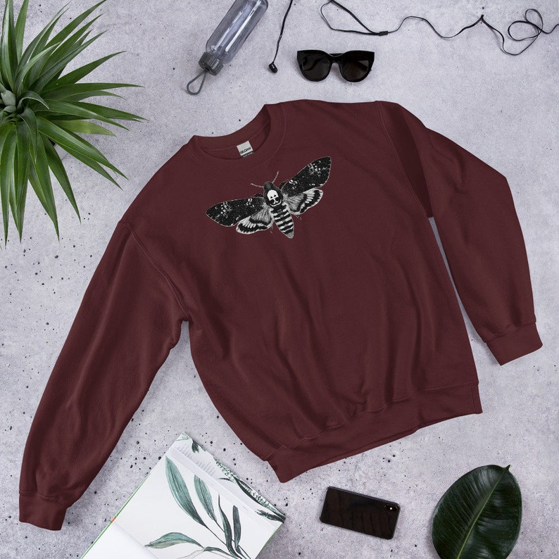 May include: A maroon sweatshirt with a black and white graphic print of a moth with a skull on its head.