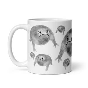 May include: White ceramic mug with a black and white illustration of multiple frogs with grumpy expressions. The frogs are all different sizes and are arranged in a random pattern on the mug.