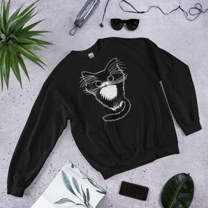 May include: Black sweatshirt with a white graphic of a cartoon cat with big eyes and a white patch on its chest.