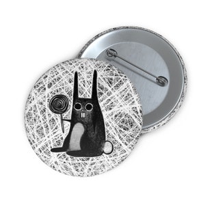 May include: A black and white button featuring a cartoon rabbit holding a lollipop. The rabbit has large eyes and a toothy grin. The background is a white and black scribble pattern.