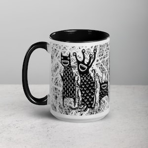 May include: White ceramic mug with a black rim and handle. The mug features a black and white illustration of three cartoon monsters with big smiles and eyes.