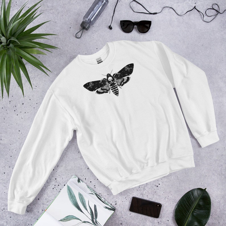 May include: White sweatshirt with a black and white graphic print of a moth with a skull on its head.