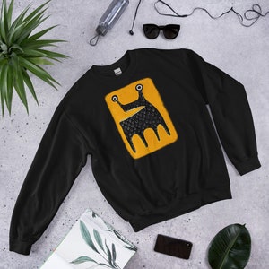 Peut inclure: Sweat-shirt noir avec un graphique carré jaune d'un monstre noir avec une grande bouche et deux yeux.