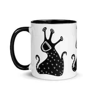 Könnte beinhalten: Weißer Keramikbecher mit schwarzem Innenraum und Griff. Der Becher zeigt eine sich wiederholende schwarz-weiße Illustration einer cartoonartigen Kreatur mit offenem Mund und mehreren Tentakeln. Das Design ist skurril und verspielt.
