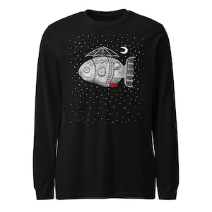 Puede incluir: Camiseta negra de manga larga con una ilustración caprichosa de una nave espacial con forma de pez con un paraguas, una luna creciente y un fondo estrellado. El pez tiene un escape rojo y una cola de código de barras.