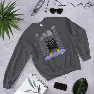 May include: A dark grey sweatshirt featuring a black cartoon character wearing yellow wellies and smiling beneath a grey rain cloud. The character is standing in a puddle of water with rain falling around them.