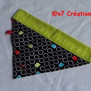 May include: A triangular fabric item with a black background and white circles, accented with green polka dots and small colorful shapes. The text "@n7 Créations" is in red. A small red loop is attached.