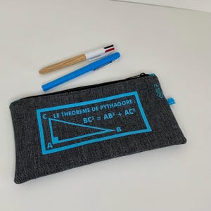 Può includere: Un astuccio grigio con cerniera nera, con il testo "LE THEOREME DE PYTHAGORE: BC² = AB² + AC²" in blu. Due penne, una blu e una con motivo legno, sono sopra. L'astuccio ha un'etichetta blu.