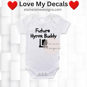 May include: White baby bodysuit with short sleeves and popper fastenings. The bodysuit features the text "Future Hyrox Buddy" in black, along with a graphic. The top of the image has the text "Love My Decals" and a website address.