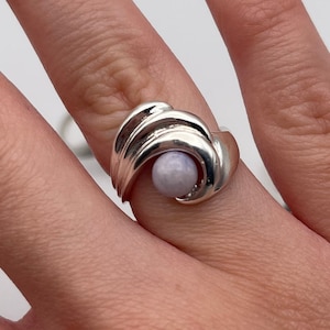 Puede incluir: Un anillo de plata con un diseño de espiral y una piedra preciosa de color púrpura claro.