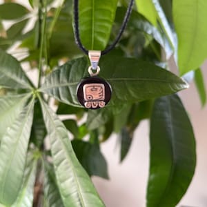 May include: A black onyx pendant necklace with a silver Mayan glyph design. The necklace is on a black cord.