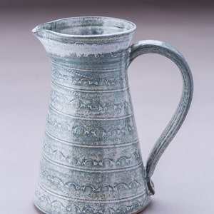 May include: A blue ceramic jug with a white rim and a decorative pattern. The jug has a wide base and a narrow neck, with a handle on one side.