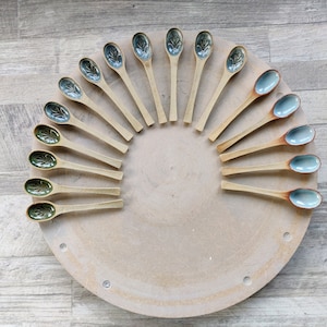 May include: A collection of 18 wooden spoons with blue and green glaze. The spoons are arranged in a semi-circle on a wooden surface.