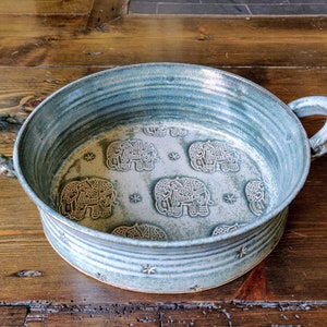 May include: A blue ceramic baking dish with two handles. The dish has a white interior with a pattern of elephants and stars.