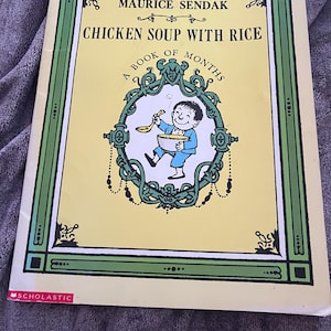 May include: A children's book titled "Chicken Soup with Rice" by Maurice Sendak. The cover features a smiling boy in blue holding a bowl and spoon, surrounded by an ornate green and white frame on a yellow background. The book is published by Scholastic.