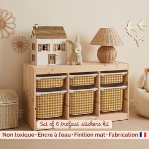 Puede incluir: Un mueble de almacenamiento de madera con seis cubos con estampado de cuadros amarillos y blancos. Una casa de muñecas, una figura de conejo y una lámpara encima. El texto "Set of 6 trofast stickers kit" es visible.