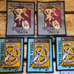 Pode incluir: Cinco patches bordados com um tema de bicicleta. Os dois patches superiores são azuis com um ciclista a andar de bicicleta. Os três patches inferiores são azuis com um anel de corrente de bicicleta e o texto "Century" e "TIERRA BELLA". O texto nos patches superiores diz "April 3, 1993" e "April 3, 1998" e "Tierra Bella". O texto nos patches inferiores diz "April 9, 1994".