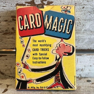 Puede incluir: Una caja vintage de trucos de magia de cartas con fondo amarillo, cartas rojas y azules y un mago de dibujos animados con una expresión de sorpresa. La caja dice "CARD MAGIC" y "The world's most mystifying CARD TRICKS with Special Easy-to-Follow Instructions".