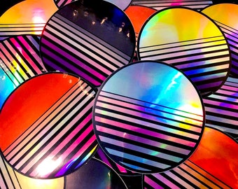 May include: A collection of iridescent holographic stickers with a retro 80s design. Each sticker features a black and white striped pattern with a single colour stripe across the centre. The colours include red, blue, yellow, and purple.