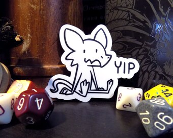 May include: A black and white sticker of a cartoon dog with the word "YIP" next to it. The sticker is on a table with several dice.