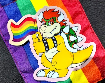 May include: A yellow and green cartoon character holding a rainbow flag. The character is wearing a black studded belt and has a spiky shell on its back. The character is on a rainbow background.