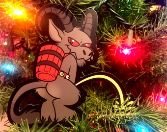 May include: A grey, cartoonish, horned creature with a red barrel on its back, is depicted in a Christmas tree bauble. The creature is standing on its hind legs and has a long, yellow tail.