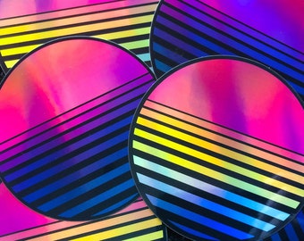 May include: Five round stickers with a holographic finish. Each sticker features a pink, blue and yellow striped design with a gradient background.