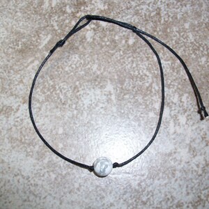 May include: A simple black cord necklace with a single white bead.