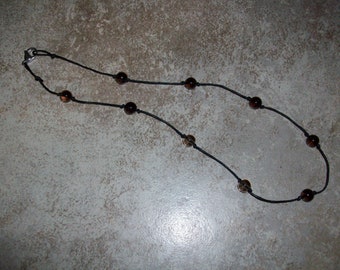 May include: A black cord necklace with brown glass beads.
