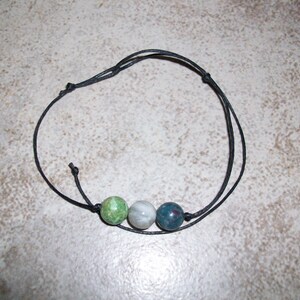 May include: A black cord bracelet with three round beads. The beads are green, white, and blue.