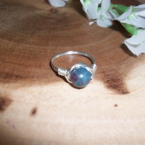 May include: A silver ring with a dark blue and green gemstone wrapped in silver wire.