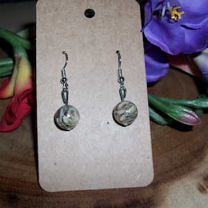 Puede incluir: Un par de pendientes de plata con colgantes redondos de color blanco y marrón.