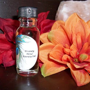 May include: A small clear glass bottle with a black cap. The bottle contains a liquid and has a white label with the text "Divinity Blend Essential Oil". The label also features a peacock feather design.